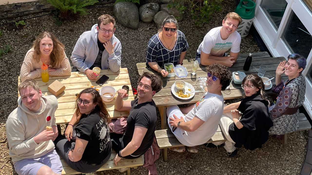 An overhead shot of a group of smiling people eating lunch on a picnic table.
